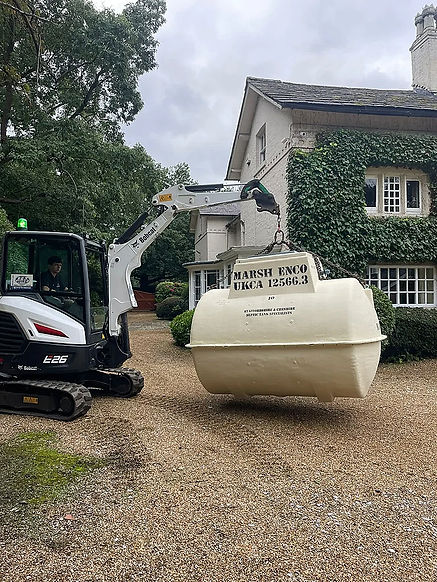 Excavator lifts Klargester wastewater treatment system near house.
