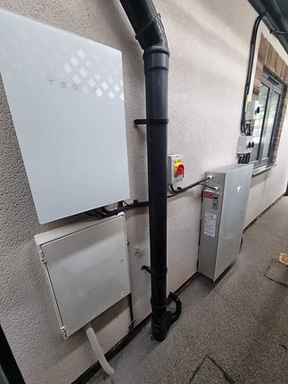 A white Tesla Powerwall and other electrical components mounted on the exterior wall of a building