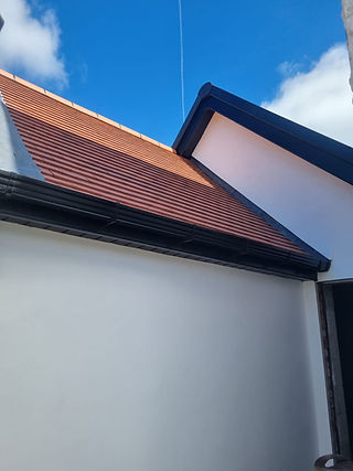 A newly tiled roof with red shingles contrasts against a bright blue sky