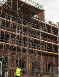 Brick building under construction with scaffolding and worker