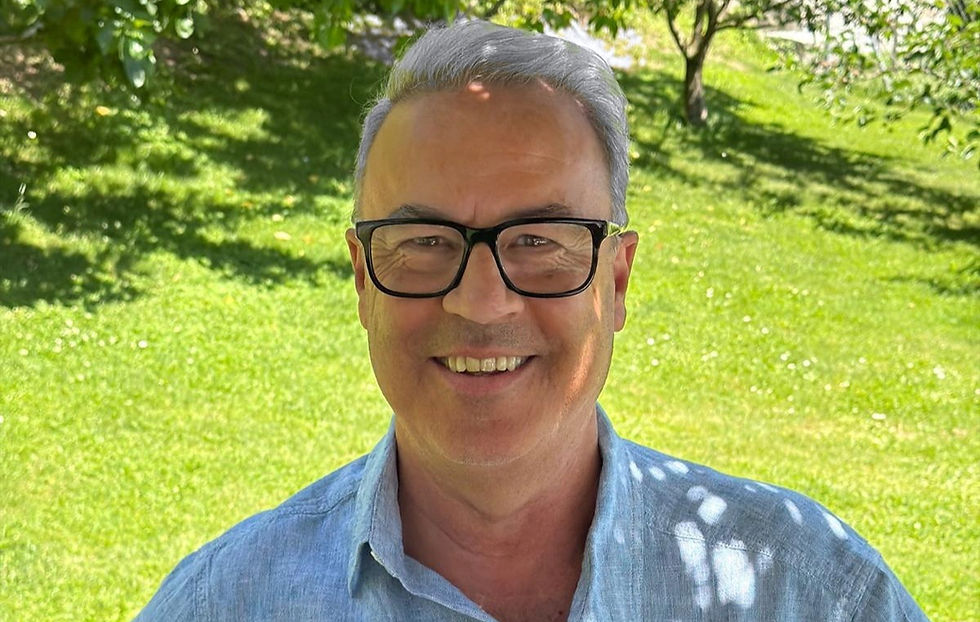 Erich Huber steht lächelnd unter einer Weinlaube, hinter ihm öffnet sich ein Weg