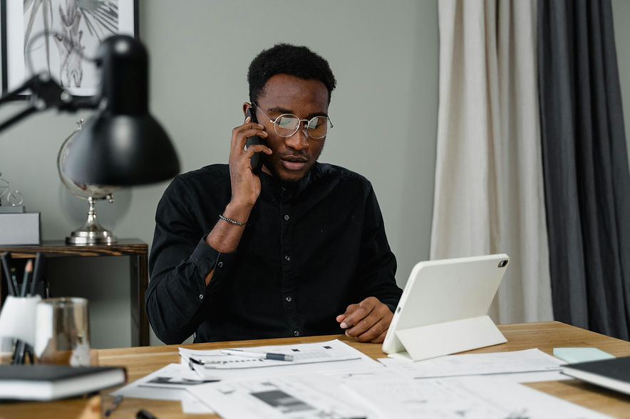 Entrepreneur reviewing documents while on the phone at a desk, representing decision-making and systems involved in building Black wealth.