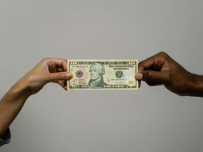 Two hands holding a $10 bill, one white hand, one black hand, seemingly fighting for the cash, plain gray background. The bill is centered, with visible text and portrait details.