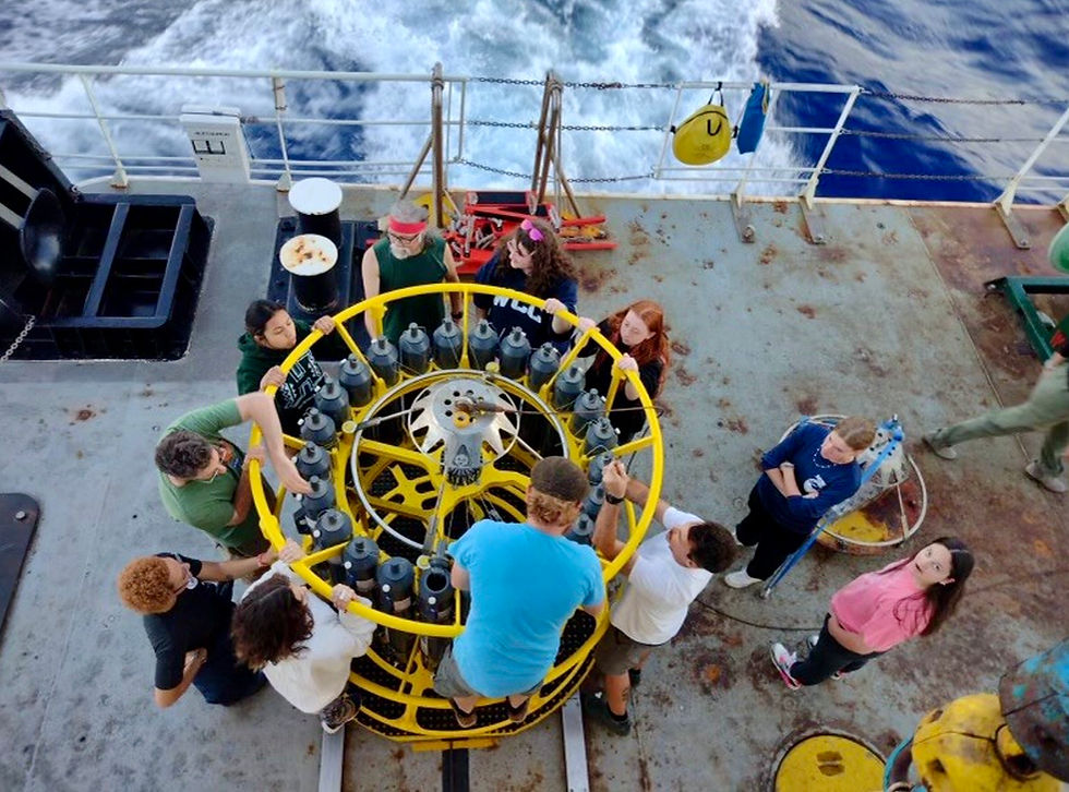 Students and scientists working around a CTD and water sampling device aboard a ship.