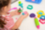 Child in a striped shirt plays with colorful playdough and molds, forming a playful creature. Bright, cheerful activity setting.