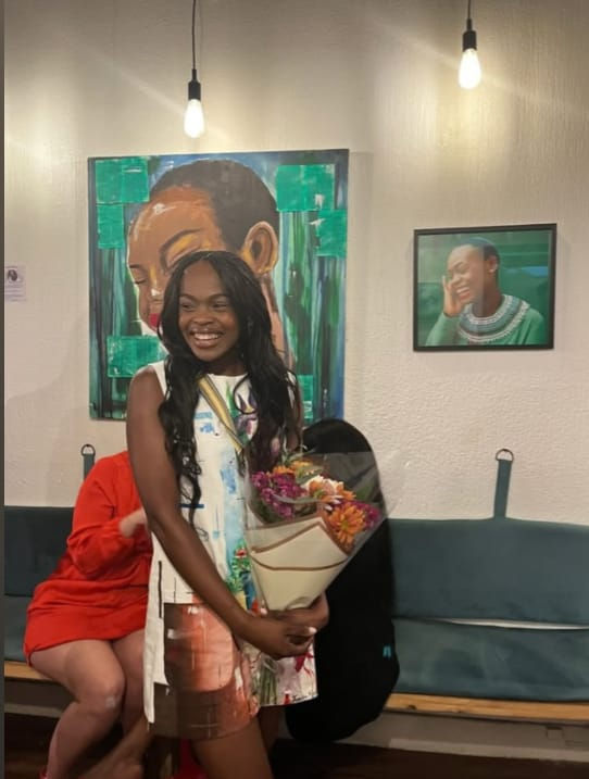 Woman smiling holding bouquet in art gallery, with colorful paintings in the background. Warm lighting creates a joyful atmosphere.