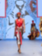 Model in red top and patterned skirt walks on fashion runway. Bold graphics on backdrop; vibrant colors create an energetic mood.
