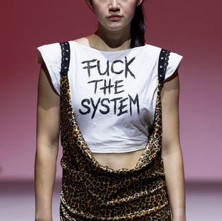 Model in white shirt and dress, outfit walks on a fashion runway against a teal background, exuding confidence and style.
