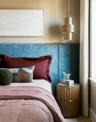 A neutral, spa-like bedroom, with a blue chambray headboard and throw pillows in wine red and earth tones
