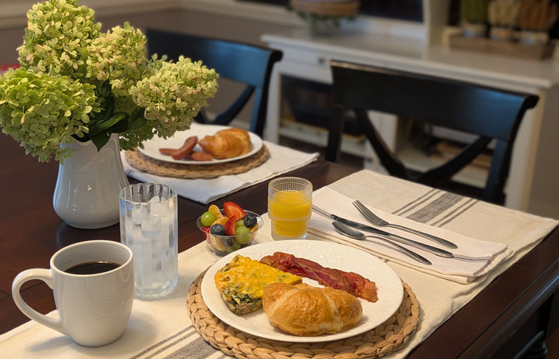 Farmhouse breakfast table set with a savory egg entrée, bacon, croissants, fresh fruit, orange juice, coffee, and hydrangeas at The Fox and The Farmhouse.