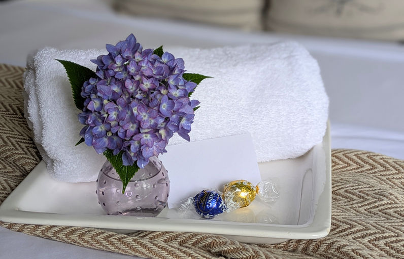 Fresh hydrangeas, folded white towels, chocolates, and a welcome note arranged on a guest bed at The Fox and The Farmhouse.