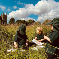 Children painting outdoors in tall grass with church behind