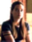Long-haired, young, brunette girl sits, wearing a navy blue ringer style tee with colorful stripes on arm bands and neck band
