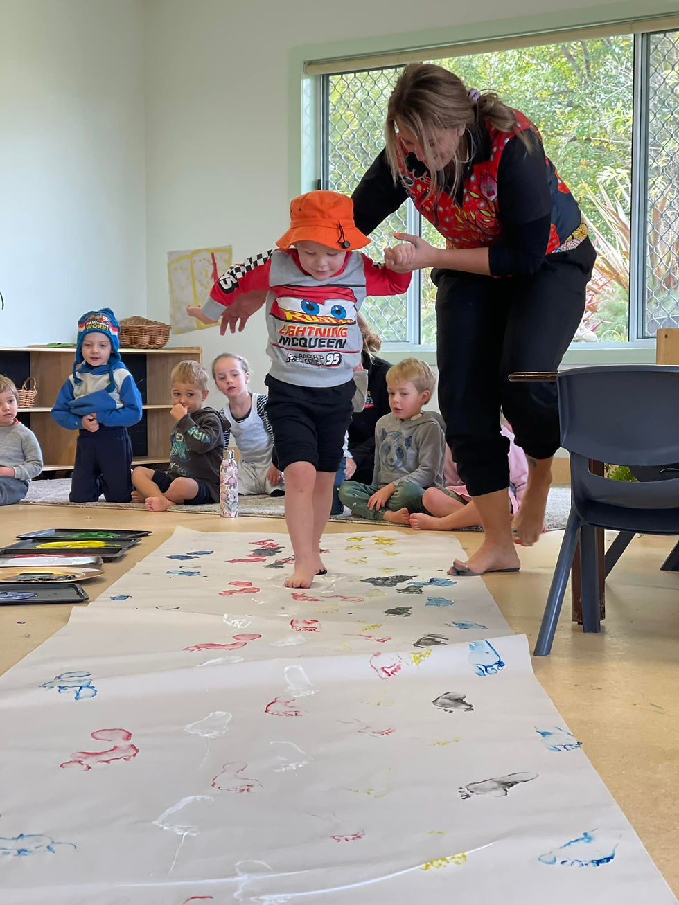  tg's uralla educator helping a young child with feet painting | TG's Child Care | Brilliant-Online