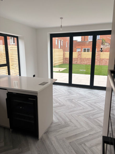 Kitchen island with white countertop, black appliance, and herringbone tile flooring, viewed through large patio doors that lead to a backyard