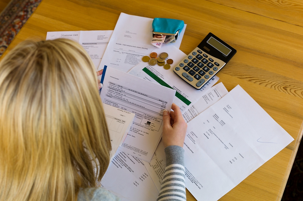 Overhead view of someone sorting household bills and debt statements with a calculator on a table.