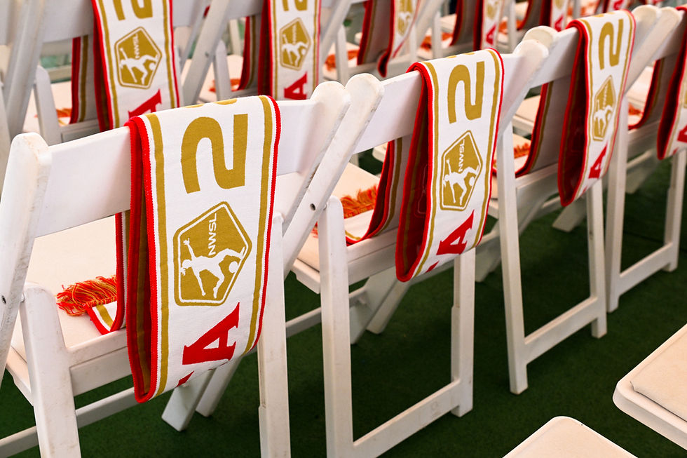 Rows of white chairs with red and yellow scarves draped over them, featuring text and logos. Green floor in the background.
