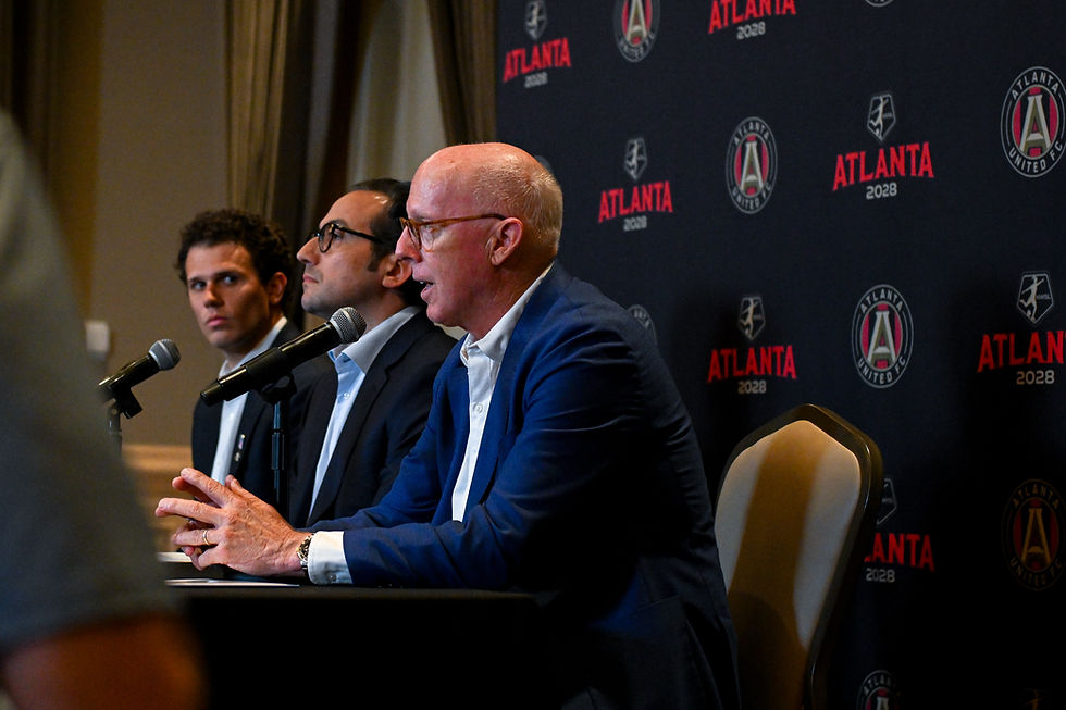 Three men at microphones during an Atlanta United FC press conference, with an Atlanta 2028 backdrop; serious mood.
