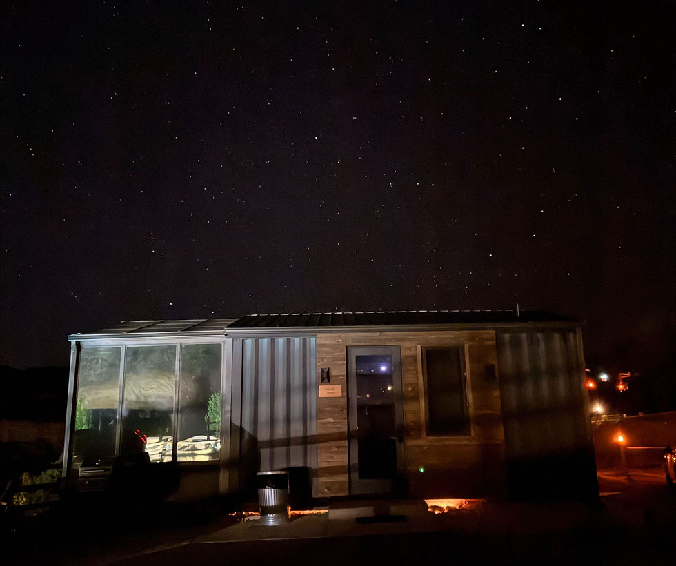 A modern container tiny home with a glass sunroom sits under a starry night sky.