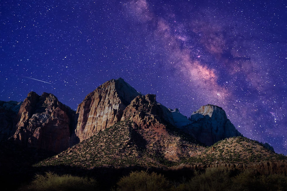 The Milky Way galaxy shines brightly in a vibrant purple night sky above rugged mountain peaks.
