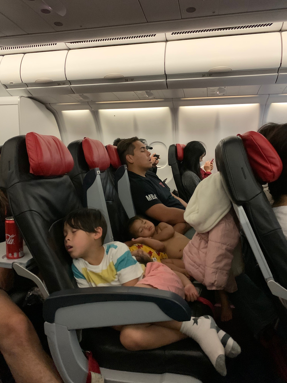 Children and dad sleep on airplane during very long flight.
