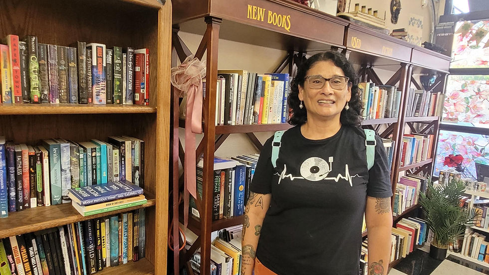 Author Renee Coloman at her favorite local bookstore. She stands beside bookshelves, smiling, amidst colorful books.