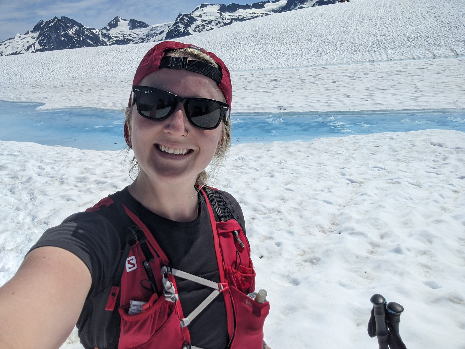 Girl in trail running gear at the top of a mountain surrounded by snow and glacial water