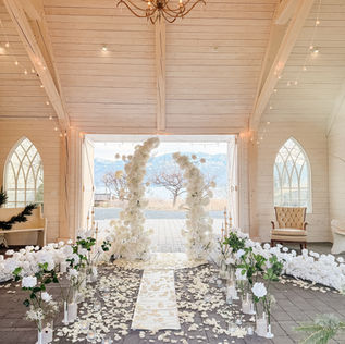 ndoor engagement proposal setup in Kelowna with white floral arches, rose petal aisle, and candlelit romantic décor