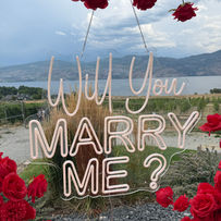 Romantic proposal setup between vineyard rows at The Gallery Winery with a red floral heart and Okanagan Lake in the distance.