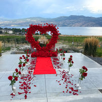 Oversized red rose heart proposal setup at The Gallery Winery on the Westside Wine Trail, with a red runway, rose petals, and Okanagan Lake views.