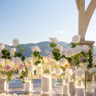 Elegant proposal setup under a lakeside pergola with Real Touch white roses, fresh baby’s breath border, and 16 oversized candles designed by Pickadilly’s in Kelowna.