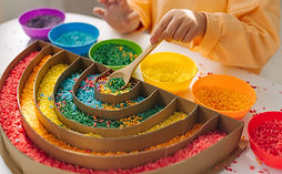 Child hands playing colored rice and make rainbow. Child filled the rainbow with bright ri
