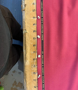 Edge of a table with inch incremented markings, a person's legs standing at the table, and wool crepe fabric pinned to the table.