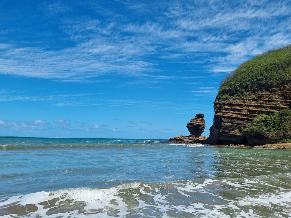 Coastal scene with a striking rock formation, Roche Percee, blue sky, and gentle waves on a sunny day. Cliff topped with greenery. Calm and serene mood.