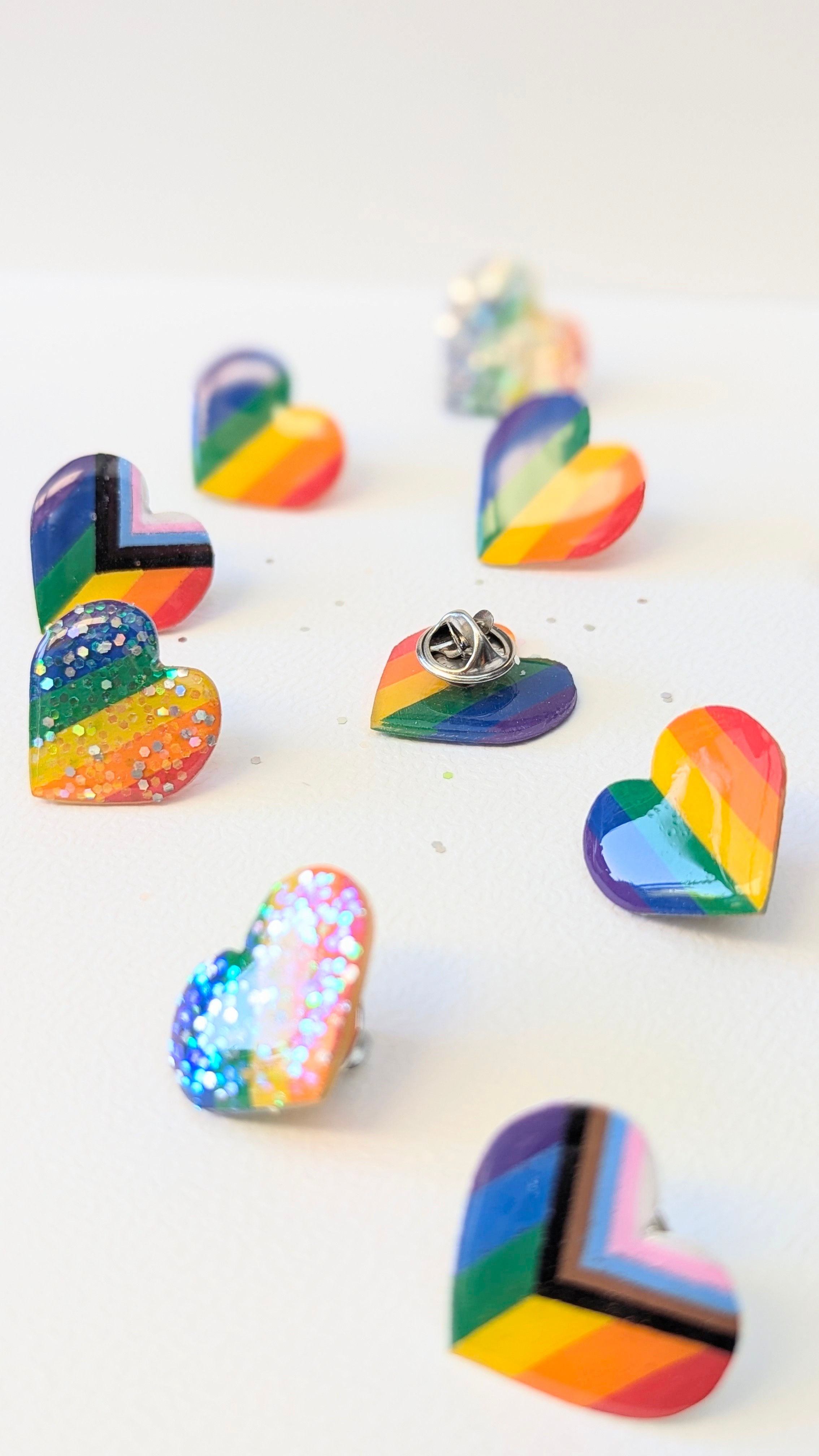 Collection de pin's Pride artisanaux en forme de cœur avec les trois modèles : classique, pailleté et Progress Pride.