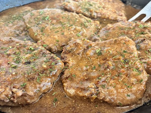 Five slices of cubed steak simmering in gravy in a cast iron skillet
