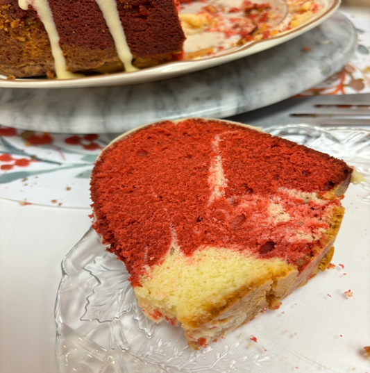 a slice of red velvet pound cake on a glass plate with the rest of the cake in the background