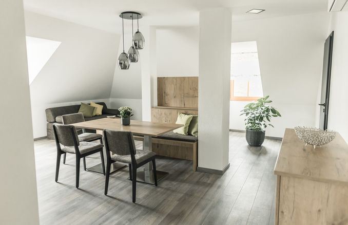 Modernes Esszimmer in der Feriensuite Waldeck mit eingebauter Holzbank, Pendelleuchten, Stühlen und Pflanze unter Dachschräge.