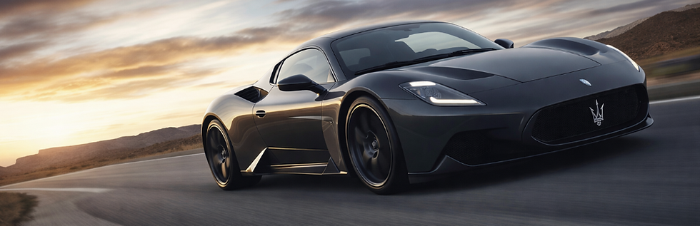Gray Maserati MC20 supercar driving on an open road at sunset.