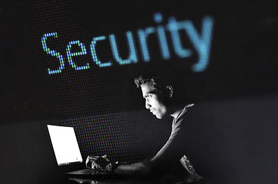 Man in a dark room looking at a laptop computer. The word "Security" floats above