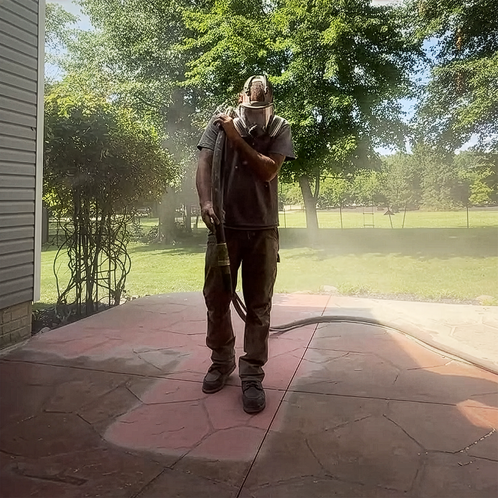 Man sandblasting old sealer from decorative concrete patio