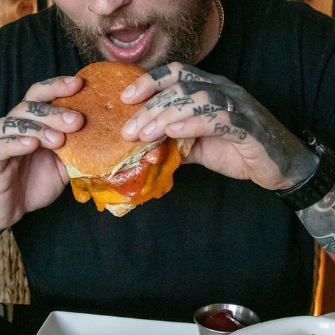 man with tattooed hands biting into a burger