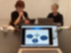 I bakgrunden syns Rosa Özgen och Astrid Hackl sittande framför sina datorer. I förgrunden syns en dator med en Powerpointbild över hur man väljer marknad.