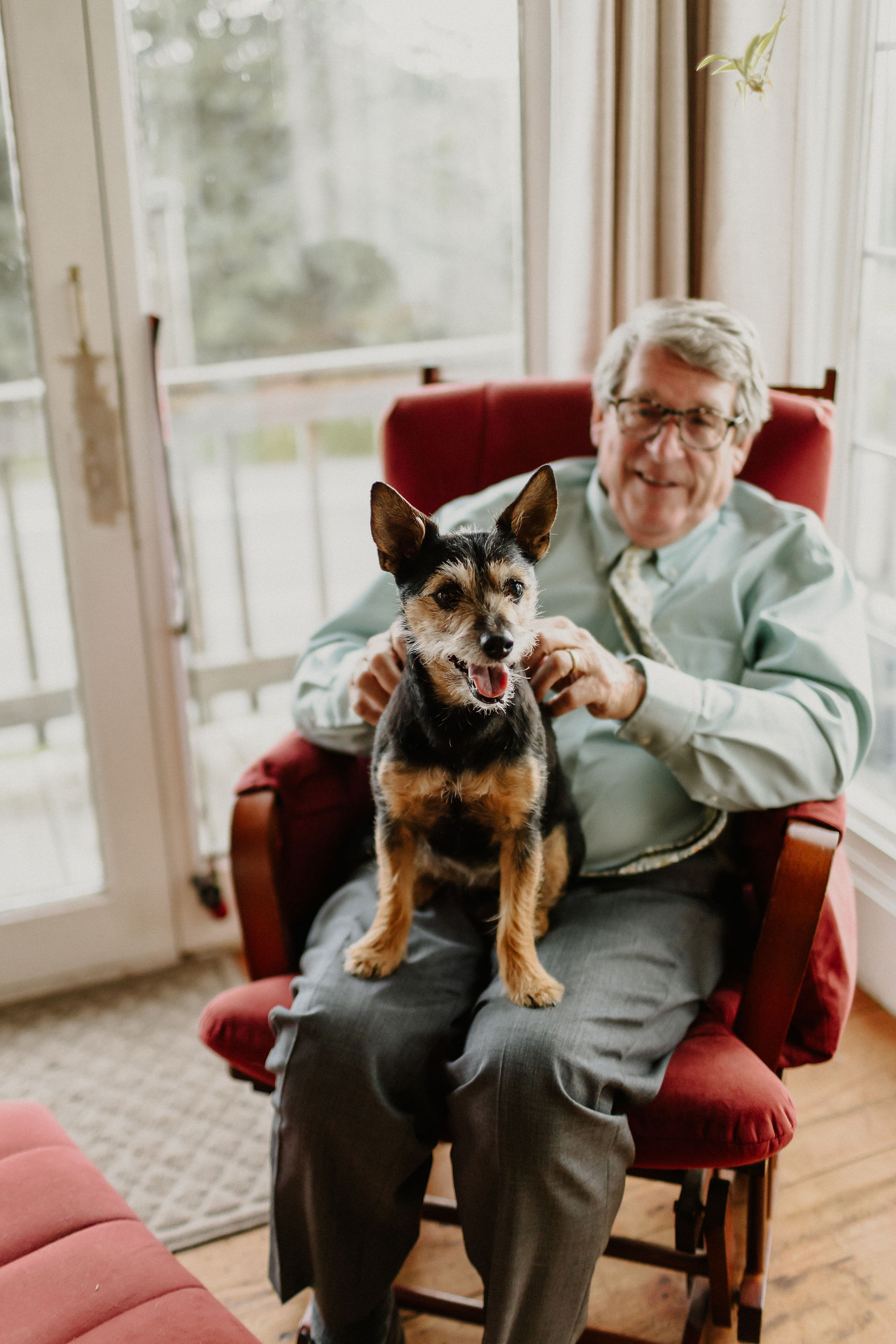 bride's father sitting on red chair with dog in his lap