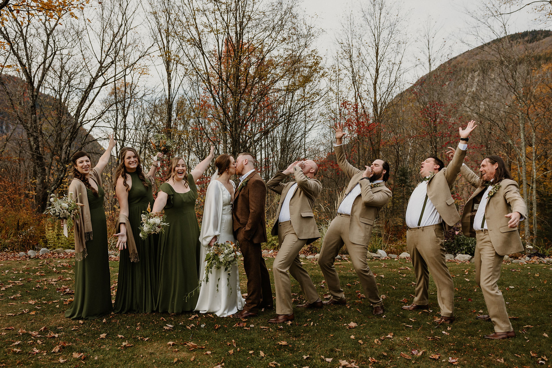 bride and groom kiss while wedding party cheers on either side of them, views of mountains the Willoughby gap behind them and fall foliage