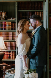 bride and groom embrace in moody library full of old books