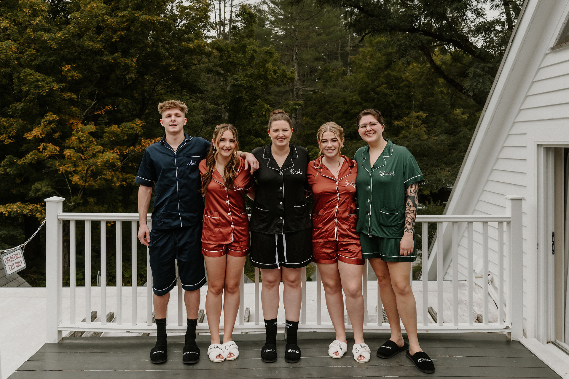 bride and bridespeople in matching satin pajamas with arms around each other on deck outside