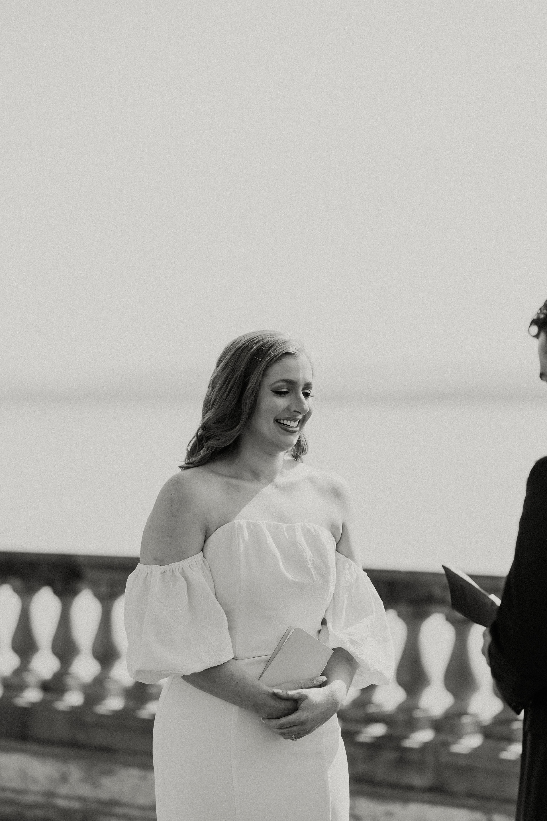 bride smiling while groom reads vows