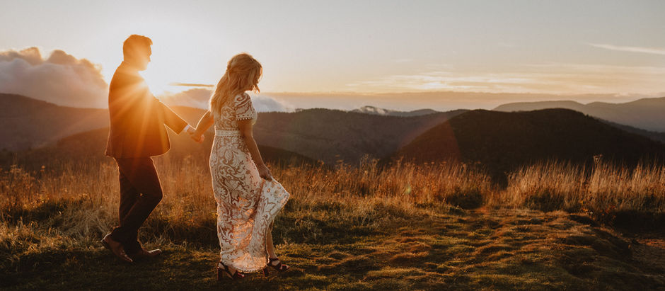 Bride and groom holding hands walking on a mountain path at sunset, glowing sunset and mountain behind them