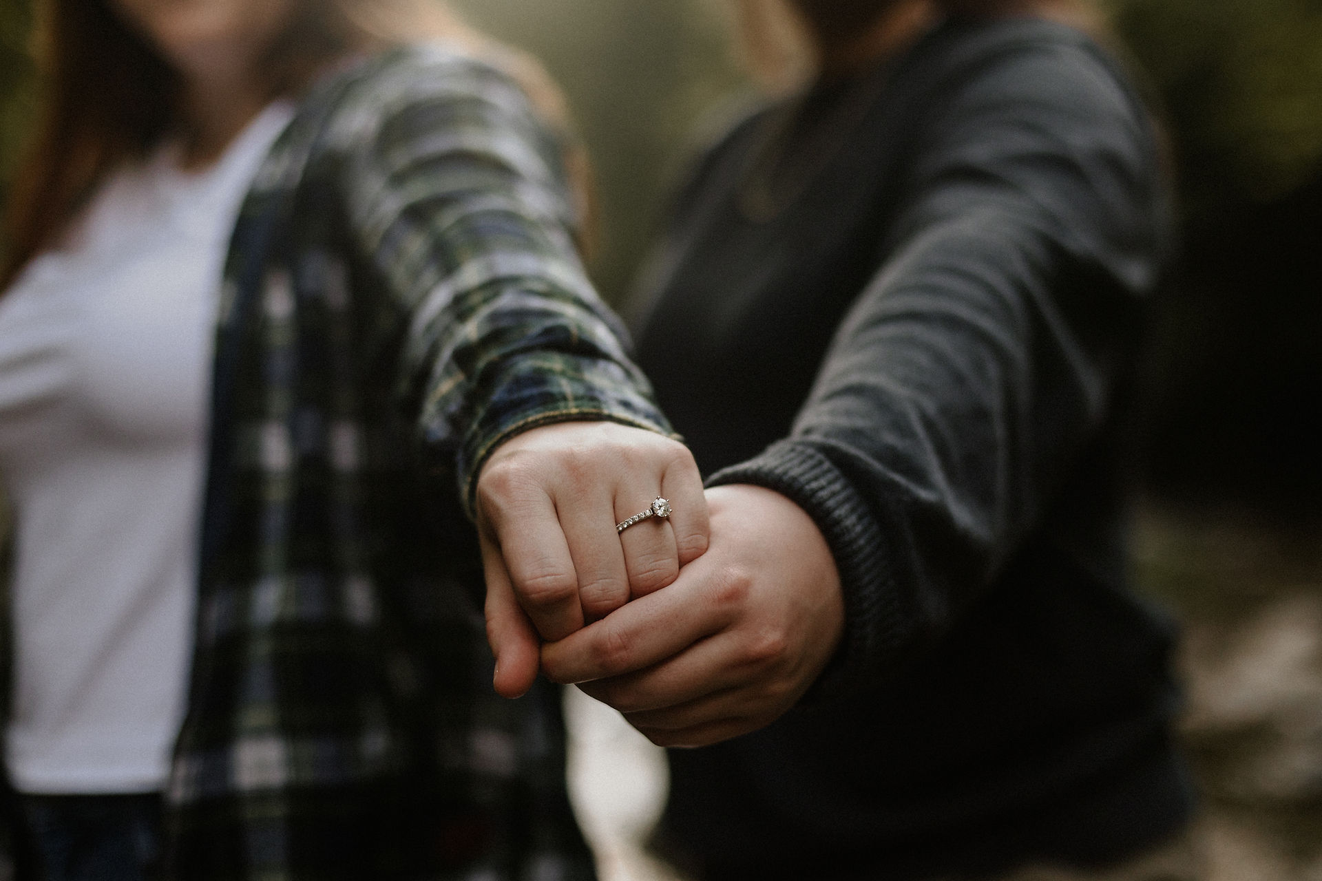 two women's hands, one holding the other out to show off an engagement ring